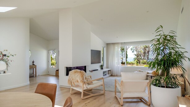Una sala de estar moderna con televisor de pantalla plana, suelo de madera y un amplio ventanal con vistas al exterior.