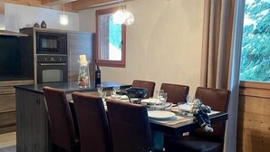 Un comedor con techo de madera, una cocina con electrodomésticos modernos y vistas a árboles por una ventana.