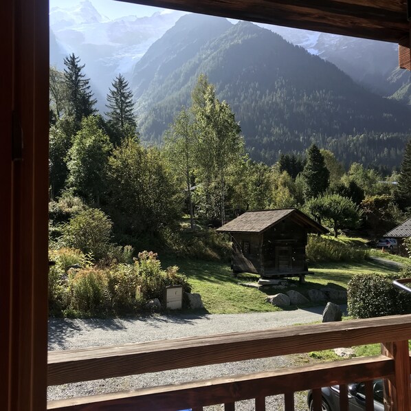 A cabin with a wooden deck, surrounded by lush greenery and mountains in the background.