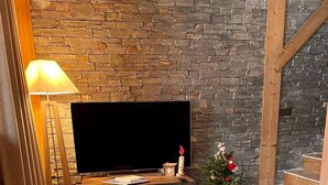 Una sala de estar acogedora con una pared de piedra, un televisor de pantalla plana sobre un soporte de madera, un pequeño árbol de Navidad y un sofá cómodo.