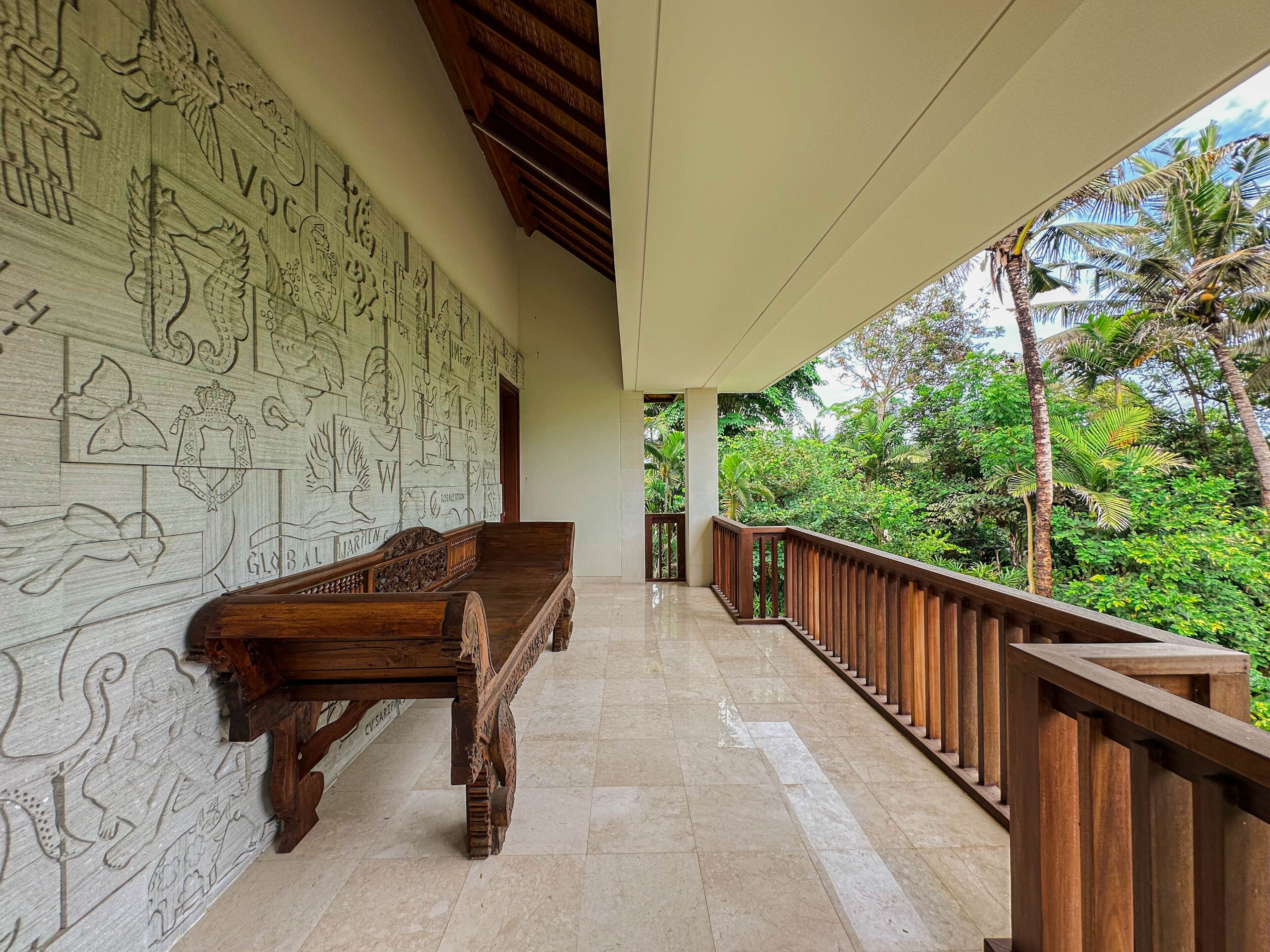 Un balcón cubierto con un banco de madera, una pared decorativa con adornos y vistas de vegetación exuberante.