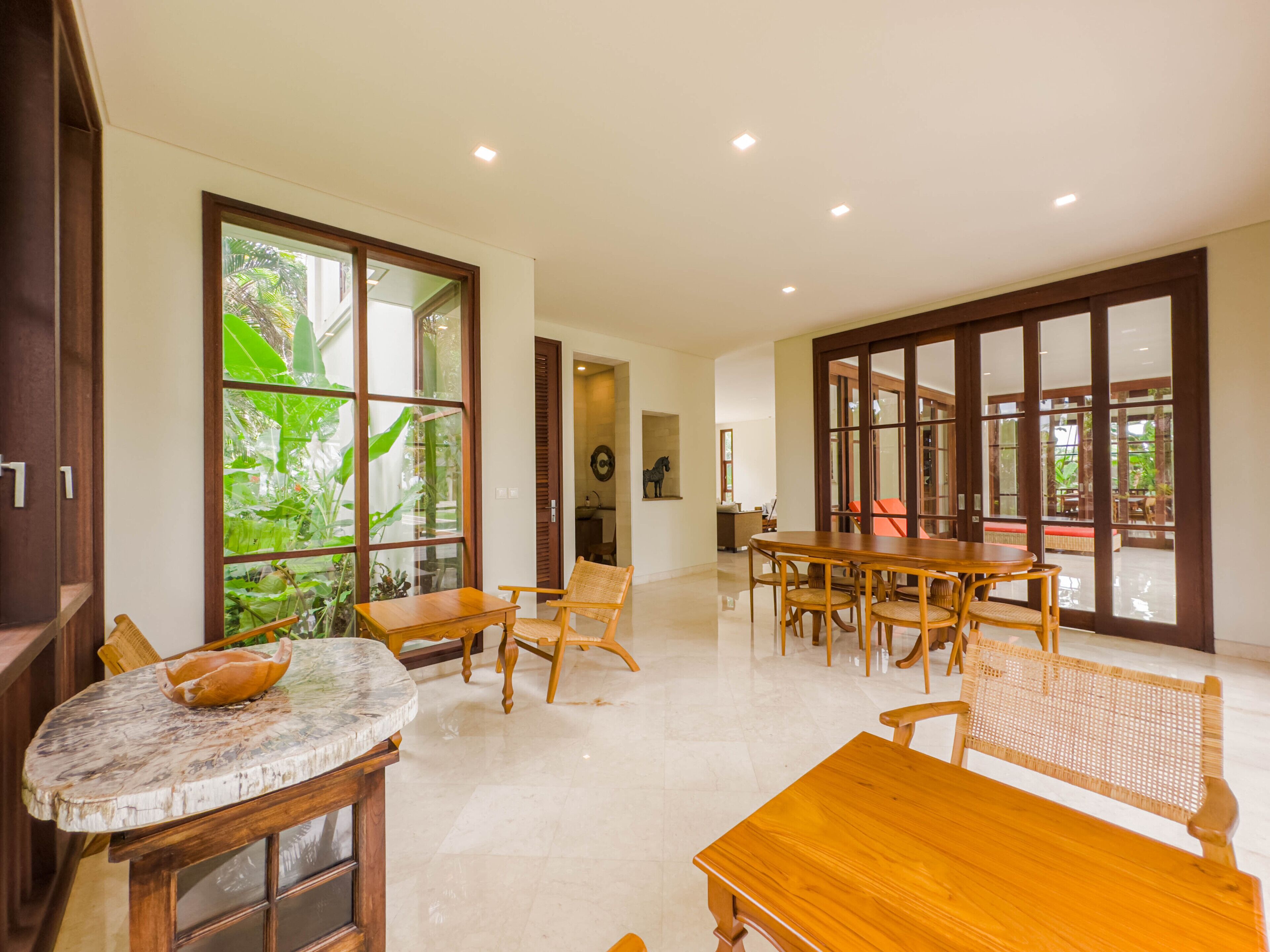 A spacious room with a large wooden dining table, wicker chairs, and a marble-top table.