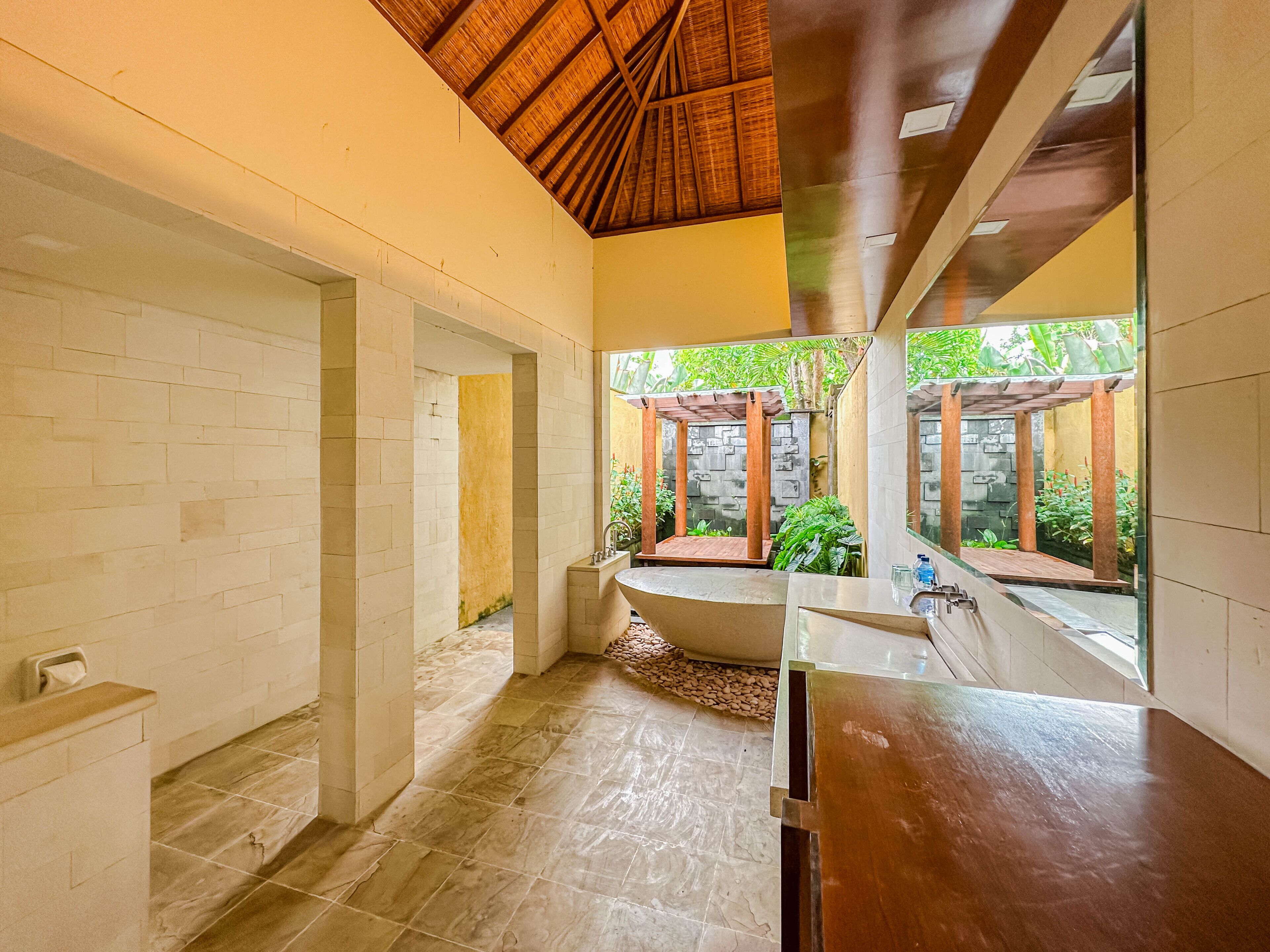 Un baño moderno con suelo de piedra, techo de madera y vistas a un jardín.