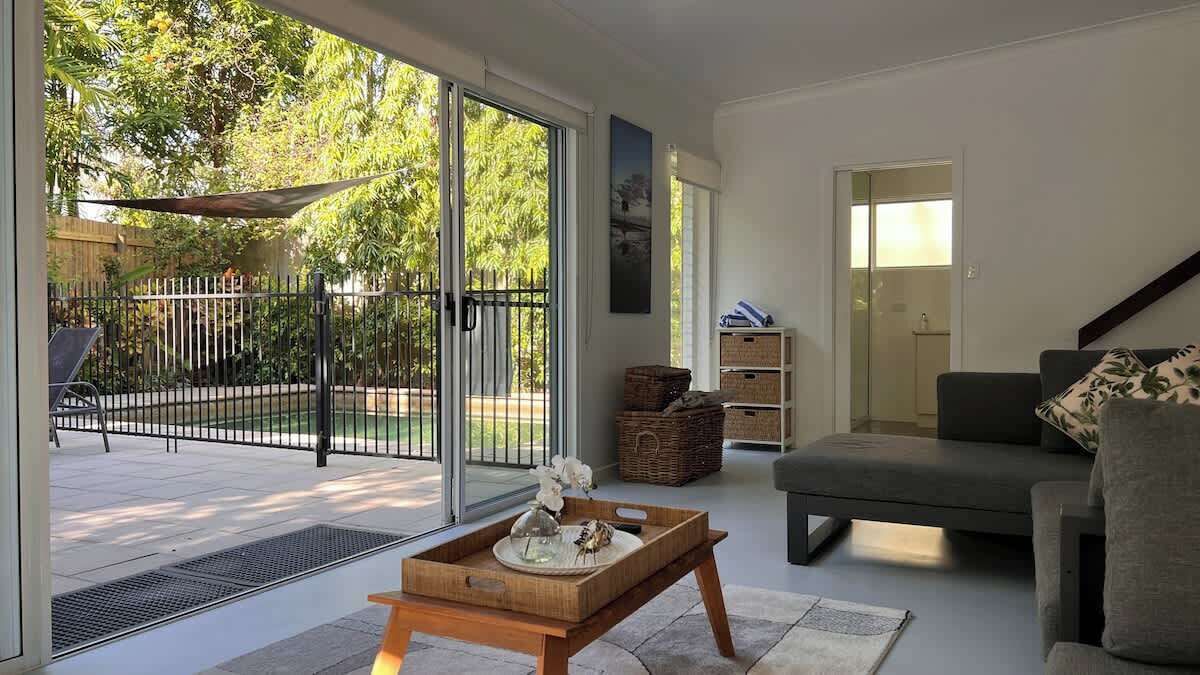 A living room with a sofa, a wooden coffee table, and a sliding glass door leading to a patio with a fence and greenery.