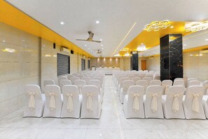 A conference room with rows of chairs, a stage, and a ceiling fan.