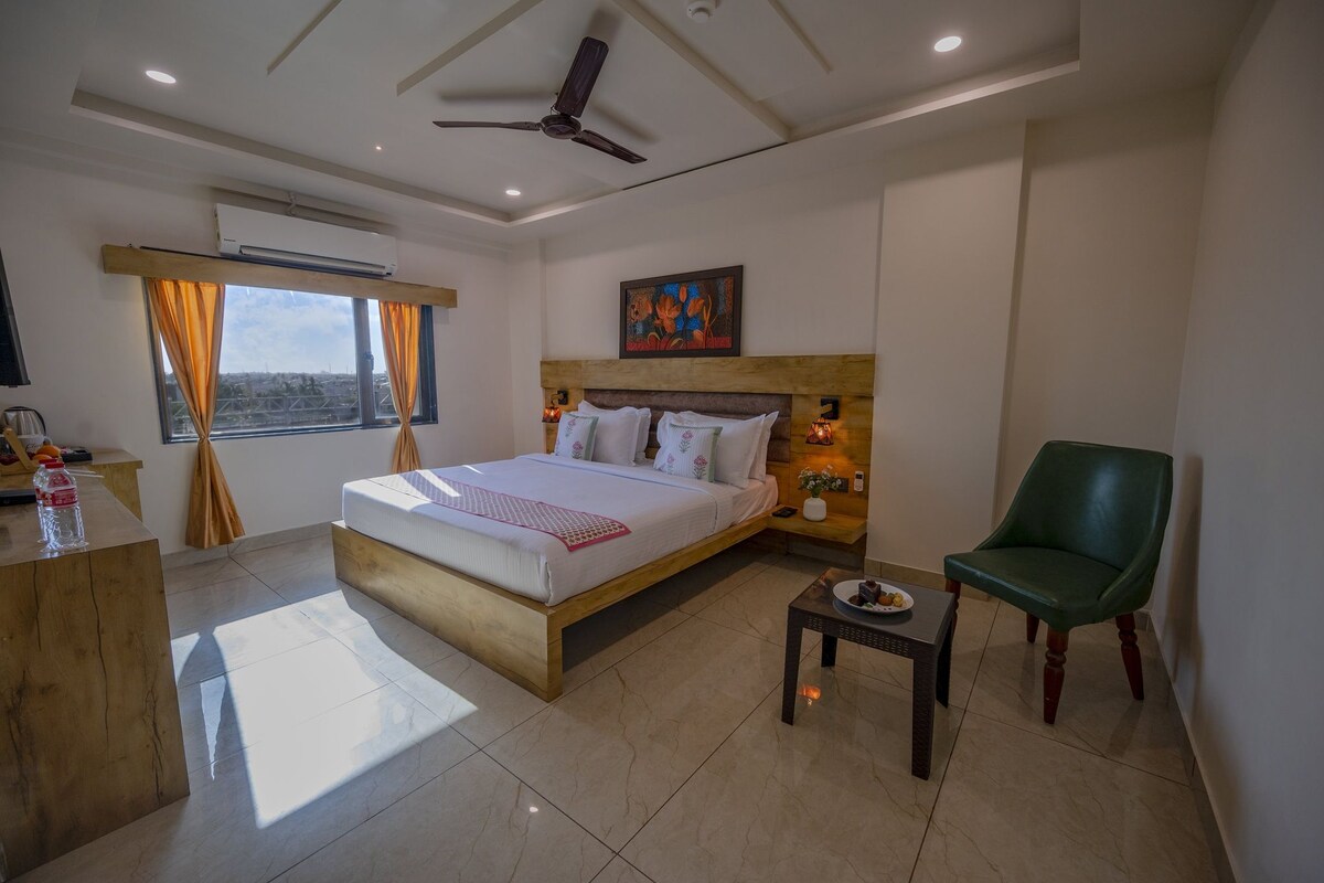 Habitación de hotel con cama, mesita de noche, silla y vista a la ciudad.