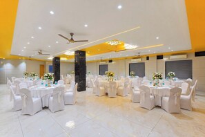 A spacious banquet hall with round tables, white chairs, and floral centerpieces. - Ginger Somnath (Veraval)