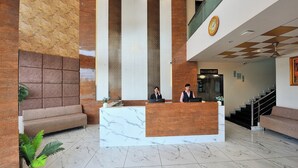 En hotellobby med en receptionsdisk, soffor, en trappa och en klocka på väggen.