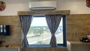A room with a large window, a flat-screen TV, and a wall-mounted air conditioner. - Ginger Somnath (Veraval)