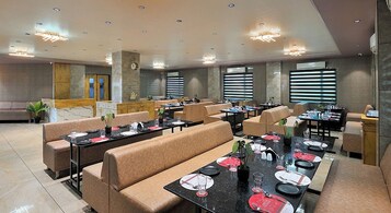 Un amplio comedor de hotel con múltiples mesas y cabinas, equipado con iluminación moderna y un ventanal que proporciona luz natural.
