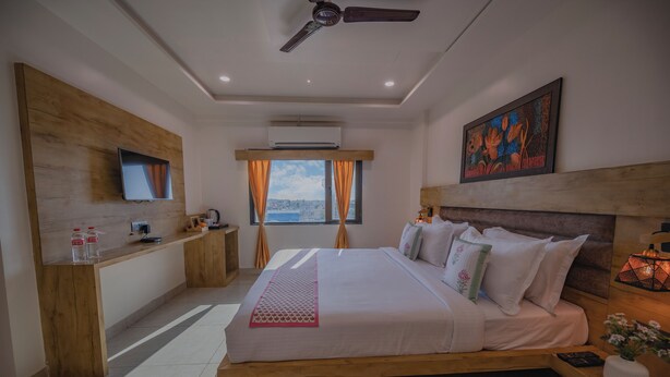 A modern hotel room with a wooden bed, a desk, a TV, and a city view. - Ginger Somnath (Veraval)