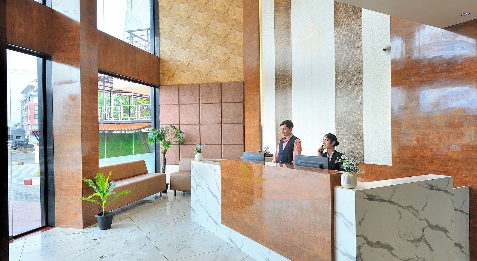 A hotel reception area with a marble reception desk, seating area, and large windows overlooking the street.