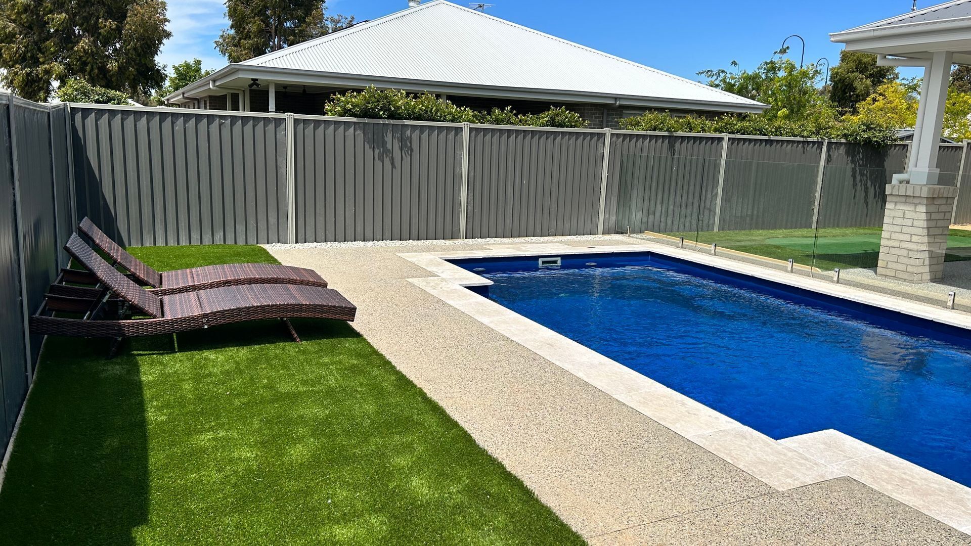 Una piscina rettangolare con bordo piastrellato, circondata da un solarium in cemento e una zona verde con due sdraio.