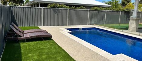 Una piscina rettangolare con bordo piastrellato, circondata da un solarium in cemento e una zona verde con due sdraio.