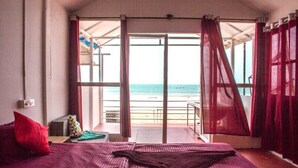 A room with a bed, a window with red curtains, and a view of the beach.