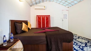 A single bed with a brown headboard, a red and white striped curtain, and a water bottle on a wooden side table.