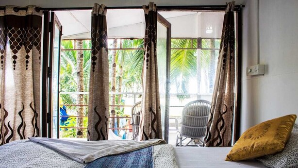 A bedroom with a bed, a window with curtains, and a view of palm trees.