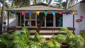 A small, single-story building with a thatched roof, surrounded by lush tropical plants.