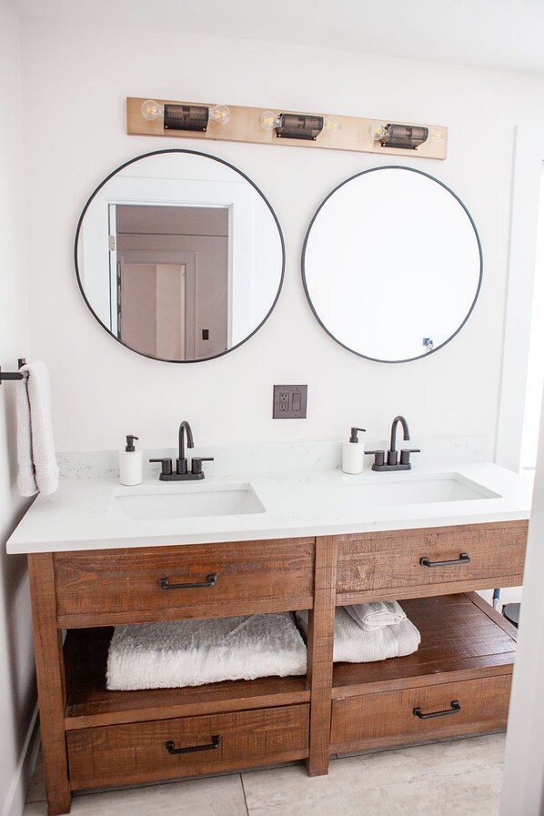 A bathroom with two sinks, two round mirrors, a wooden vanity, and a towel rack. - Updated Campus Home (Eugene)