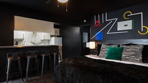 Een moderne hotelkamer met een zwart-wit kleurenpalet, een bar met krukken, een groot bed met een zachte vloerkleed en een geometrisch kunstwerk aan de muur.