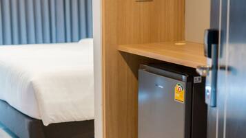 A compact hotel room with a bed, a small kitchenette with a refrigerator, and a wooden shelf.