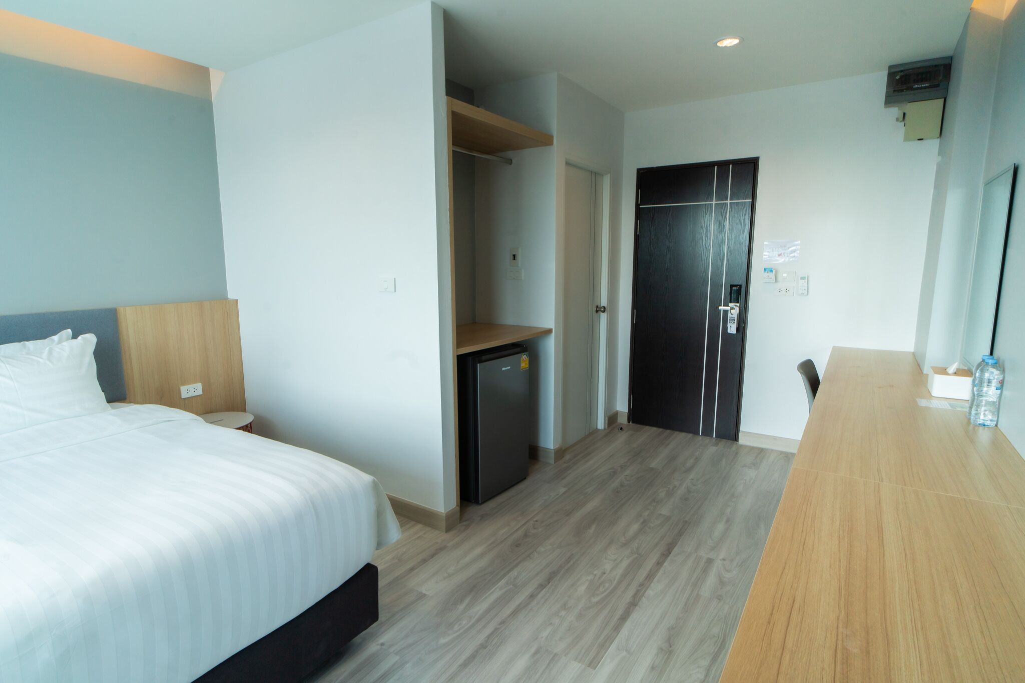 Une chambre d’hôtel comprenant un lit, un petit réfrigérateur, un bureau en bois et une porte donnant sur un placard.