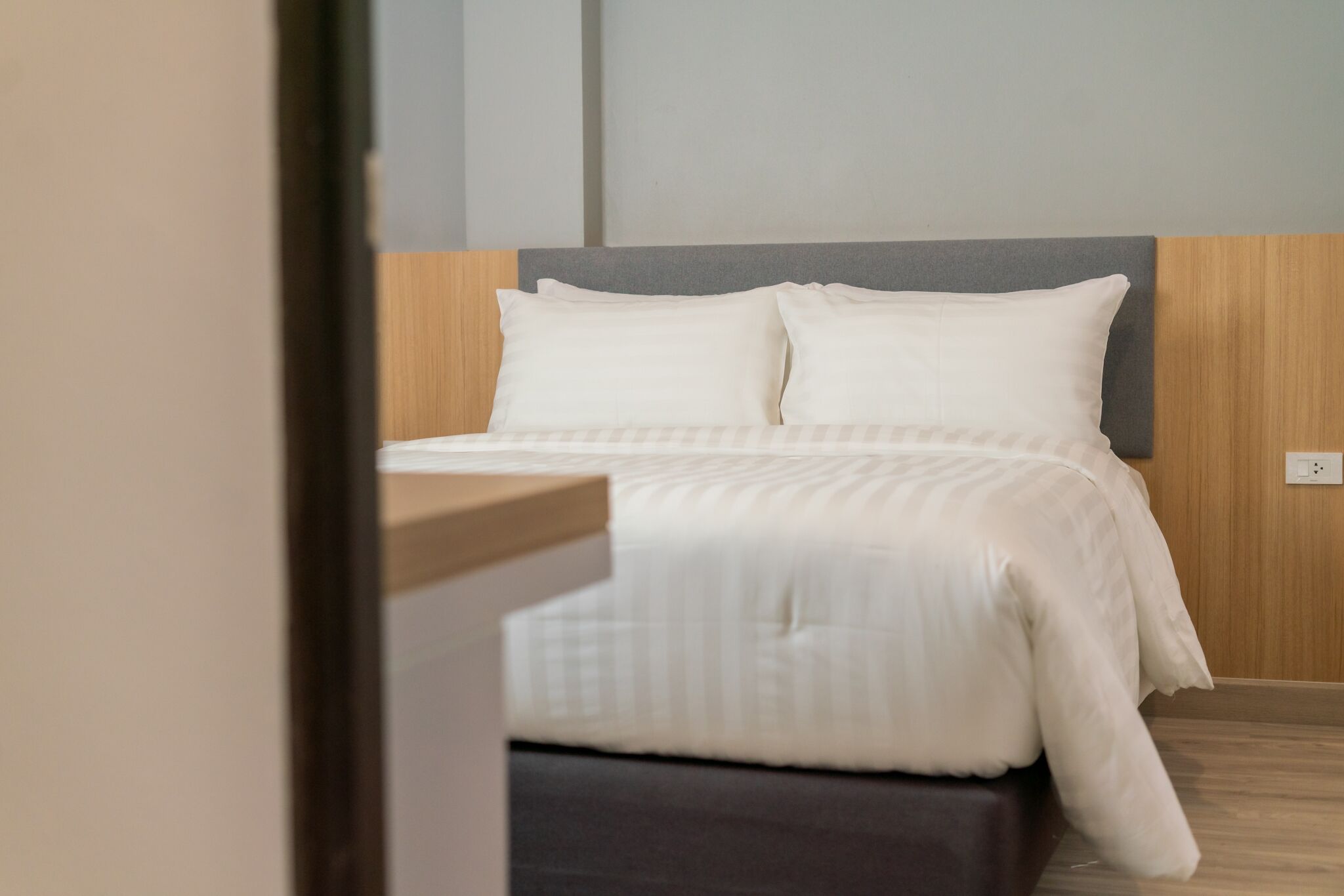 Una cama bien hecha con ropa blanca y un cabecero gris en una habitación de hotel moderna.