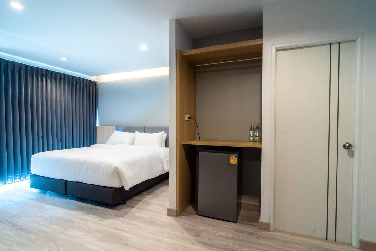 A modern hotel room with a large bed, a small refrigerator, and a wardrobe.