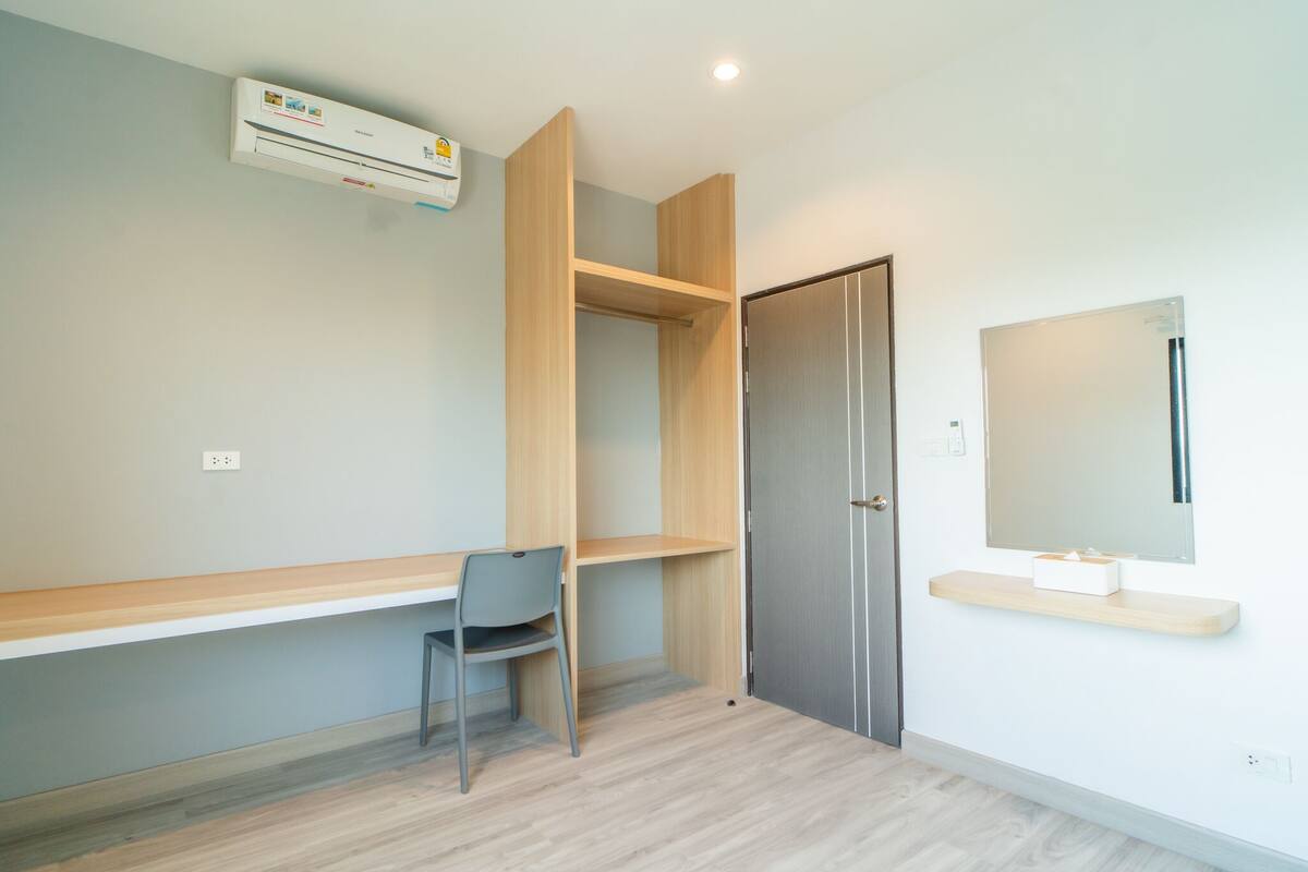A room with a desk, chair, wardrobe, and a mounted mirror.