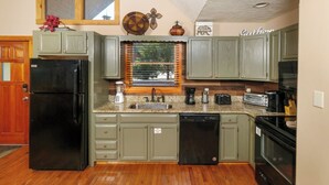A kitchen with green cabinets, a black refrigerator, a dishwasher, and a window with blinds. - Smoochin' Moose - Cozy comfort in lush surroundings! (Pigeon Forge)