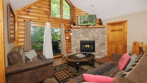 A log cabin interior with a stone fireplace, a television mounted above it, and a cozy seating area with a coffee table. - Smoochin' Moose - Cozy comfort in lush surroundings! (Pigeon Forge)