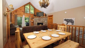 A cozy cabin interior with a dining table set for four, a fireplace, and a large window overlooking greenery. - Smoochin' Moose - Cozy comfort in lush surroundings! (Pigeon Forge)