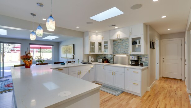 A modern kitchen with white cabinetry, a central island, pendant lights, and a view to the outside. - Saulsbury Guest House & Wellness Retreat w/ Sauna (Wheat Ridge)