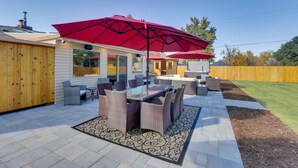 A patio area with a glass-top table and chairs, a red umbrella, and a wooden fence. - Saulsbury Guest House & Wellness Retreat w/ Sauna (Wheat Ridge)