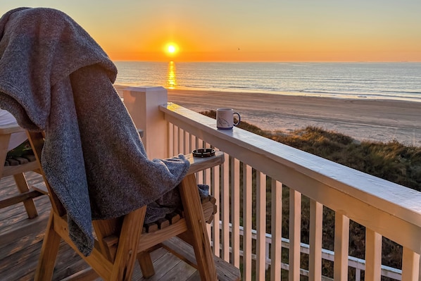 A wooden deck with a chair and a mug, overlooking a beach at sunset. - Games, Grills + Path to Ocean! Crystal Beach Haven (Crystal Beach)