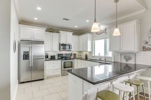 A modern kitchen with white cabinets, stainless steel appliances, and a large island with bar stools. - Games, Grills + Path to Ocean! Crystal Beach Haven (Crystal Beach)