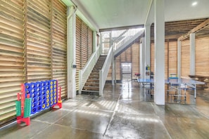A spacious interior with a staircase leading to upper levels, a blue and red game board, and tables with metal frames. - Games, Grills + Path to Ocean! Crystal Beach Haven (Crystal Beach)