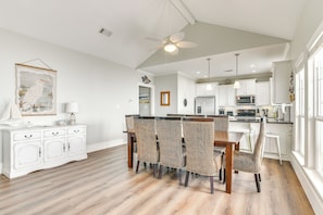 A spacious kitchen with white cabinetry, a dining area with wicker chairs, and a ceiling fan. - Games, Grills + Path to Ocean! Crystal Beach Haven (Crystal Beach)