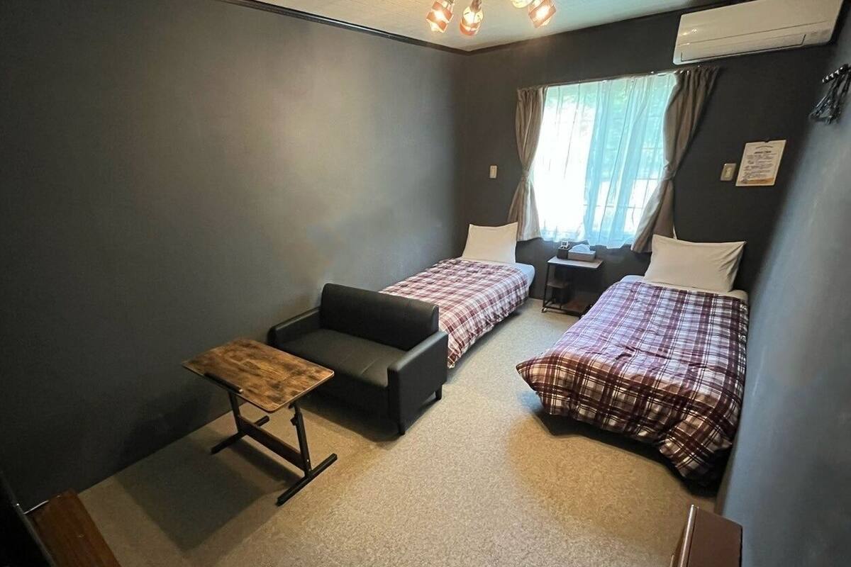 Een kleine, functionele kamer met twee bedden, een slaapbank en een tafeltje.