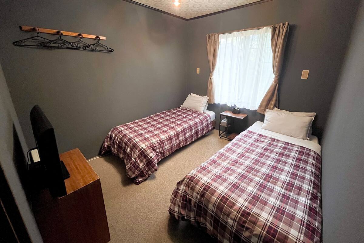 Een compacte, verzorgde kamer met twee eenpersoonsbedden, een houten dressoir, een bureau en een kapstok.