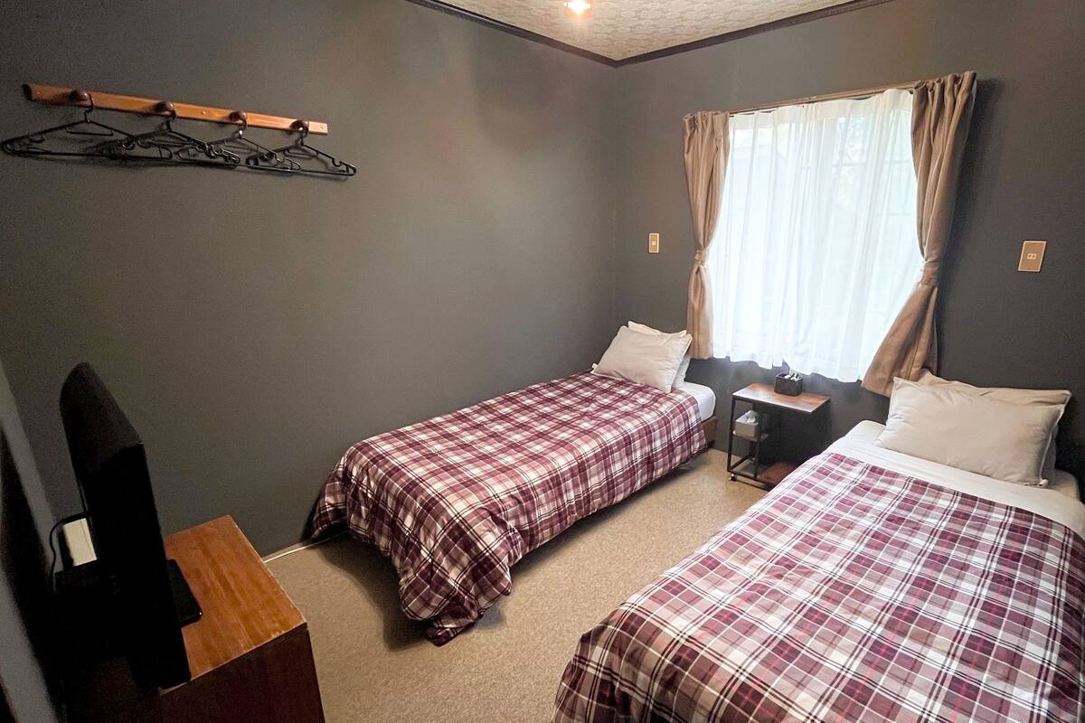 Een kamer met twee bedden, een bureau, een stoel, een kapstok en een raam met gordijnen.