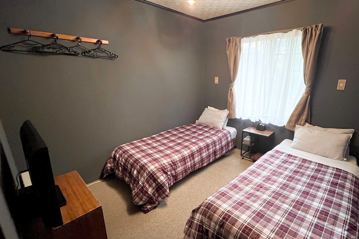 Une chambre avec deux lits, un bureau, une chaise, un porte-manteau et une fenêtre avec des rideaux.