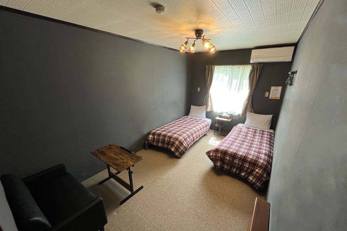 Een kleine, zwak verlichte kamer met twee bedden, een tafeltje en een bureau.