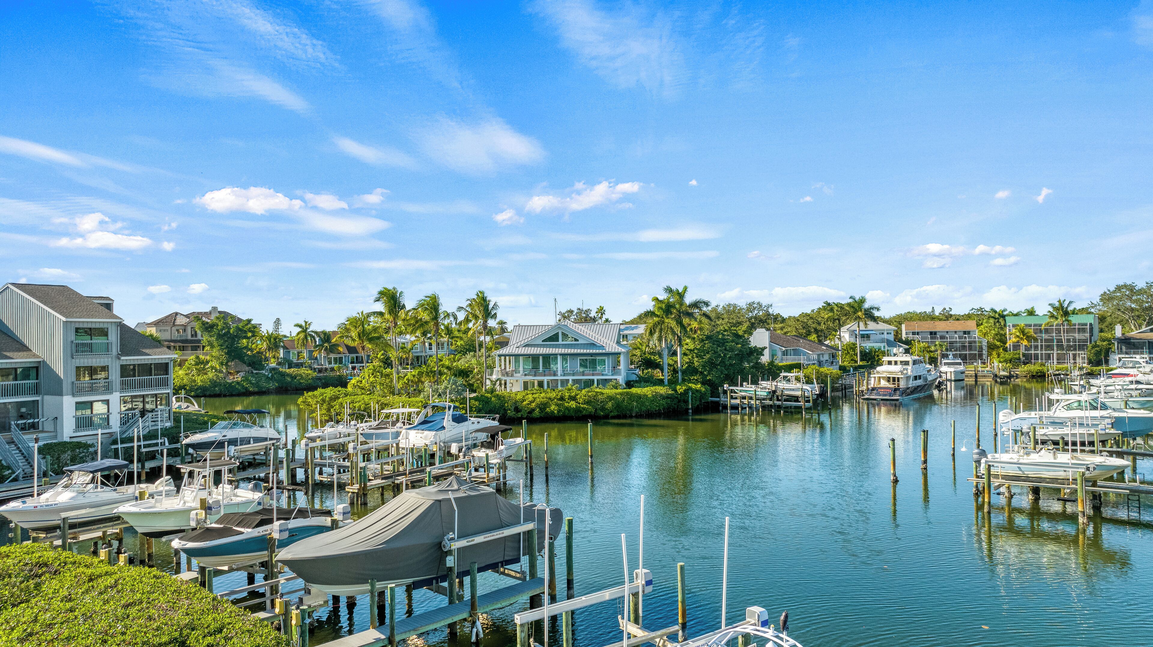 A marina with boats docked, surrounded by residential buildings and palm trees.