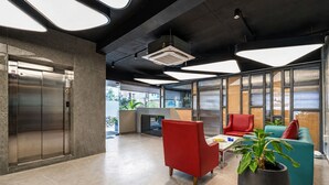 A modern lobby with a large elevator, seating area with red and teal chairs, and a large potted plant. - Eminent Suites & Apartments (Hyderabad)