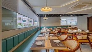 A modern restaurant with long communal tables, cushioned booths, and hanging pendant lights. - Eminent Suites & Apartments (Hyderabad)