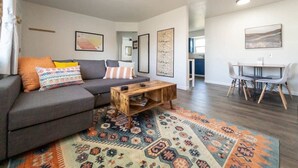 Un salon moderne avec un canapé gris, une table basse en bois et un tapis à motifs.