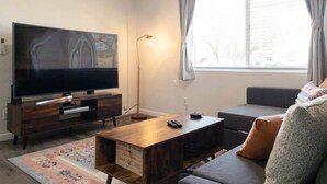 Un salon avec un téléviseur à écran plat posé sur un meuble en bois, un lampadaire, un canapé et une table basse.