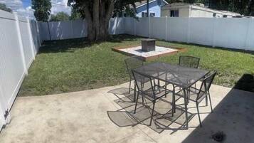 A backyard with a patio table and chairs, a fire pit, and a small garden area.