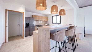 Een moderne keuken met een centraal kookeiland, roestvrijstalen apparatuur en rieten barstoelen.